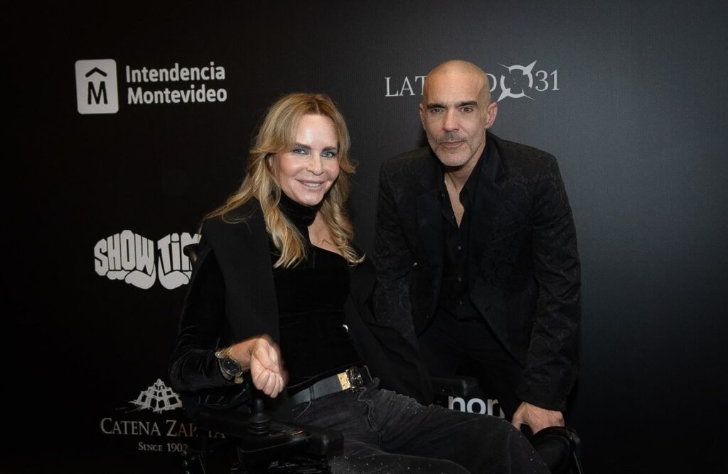 Mujer rubia y hombre de negro frente al panel de sponsors – Renato Papiccio Runway, Sofitel Carrasco
