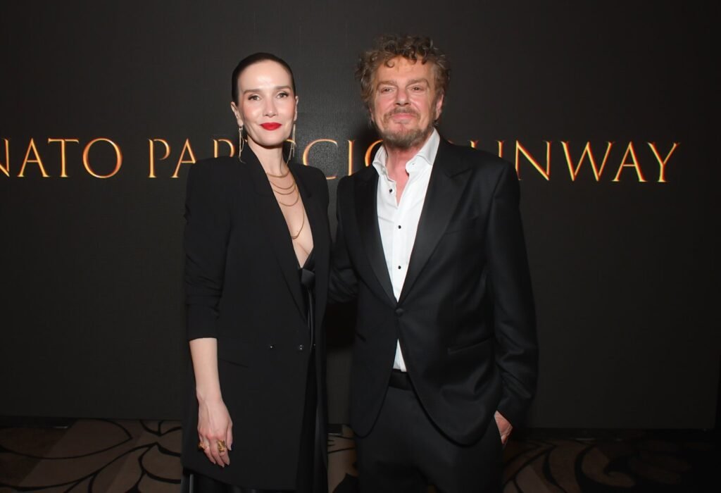Mujer de traje negro y hombre de saco frente al cartel del evento – Renato Papiccio Runway, Sofitel Carrasco